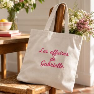 Tote bag personnalisé « Les affaires de Gabrielle », posé sur une chaise en bois dans une ambiance fleurie.